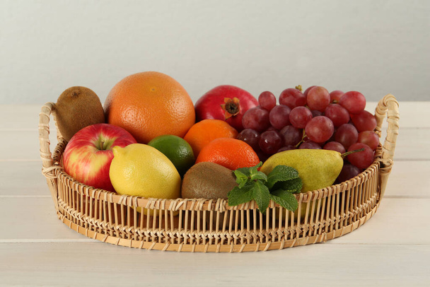 Fresh ripe fruits in wicker tray on white wooden table - Photo, Image