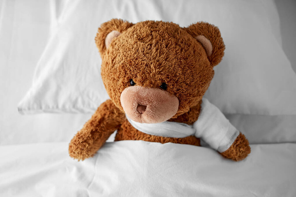ill teddy bear toy with bandaged paw in bed - Valokuva, kuva