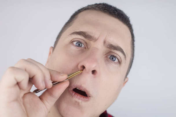 Man pulls out his nose hair with tweezers. Close-up of male hygiene products. Isolated on white background. The male looks at the screen as if in a mirror. - Foto, Bild