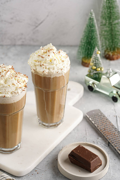 Two tall glasses with cold coffee drink frappe - iced cappuccino with whipped cream on a marble board and christmas ornaments and decoration - Photo, Image