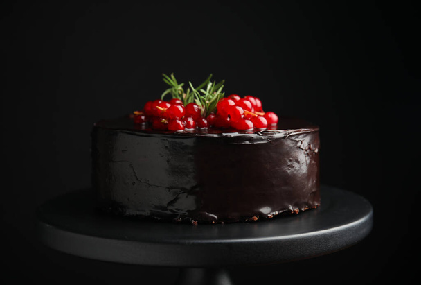Tasty homemade chocolate cake with berries and rosemary on dessert stand against black background - Fotoğraf, Görsel