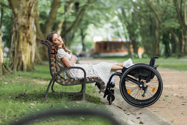 Disabled woman sitting on bench near her wheelchair at park - Φωτογραφία, εικόνα