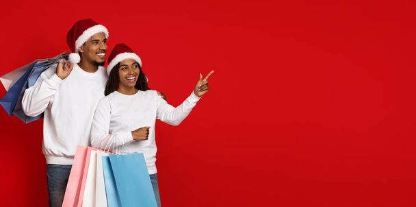 Positive black couple with shopping bags pointing at copy space - Photo, Image