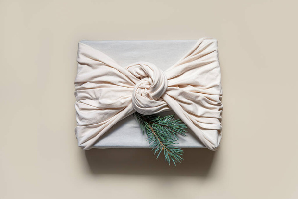 Regalo de Navidad en tejido de algodón beige con ramitas de abeto. Estilo furoshiki tradicional japonés. Envoltura de regalo de cero residuos. Concepto de diseño sostenible. - Foto, Imagen