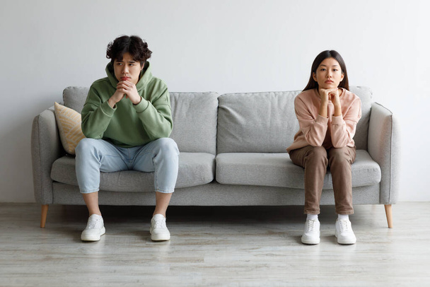Stubborn young Asian couple sitting on opposite sides of couch in silence after fight, indoors - Fotó, kép