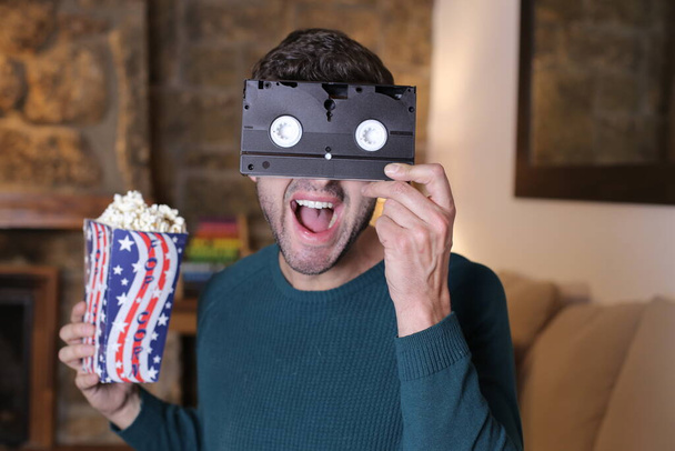 close-up portrait of handsome young man with vhs cassette and popcorn at home - Foto, Bild