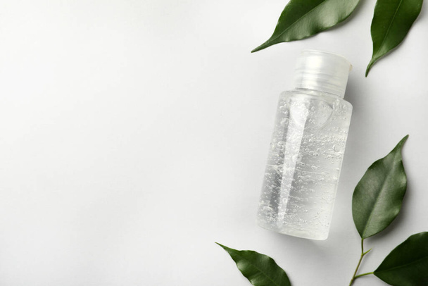 Bottle of cosmetic gel and green leaves on white background, flat lay. Space for text - Foto, Bild