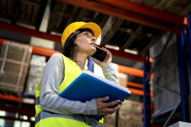 Adult caucasian woman talking by mobile phone in warehouse                                - Photo, Image
