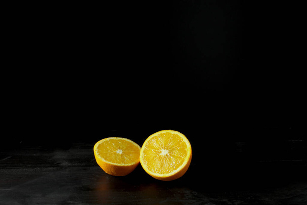 A closeup of a vibrant orange cut in half on a black background - Foto, afbeelding