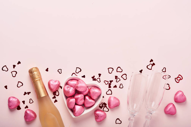 Valentines day greeting card with champagne bottle, tow glasses, chocolate hearts and gift box on pink background. Top view with space for greetings. Greeting card with copy space. - Foto, Imagem