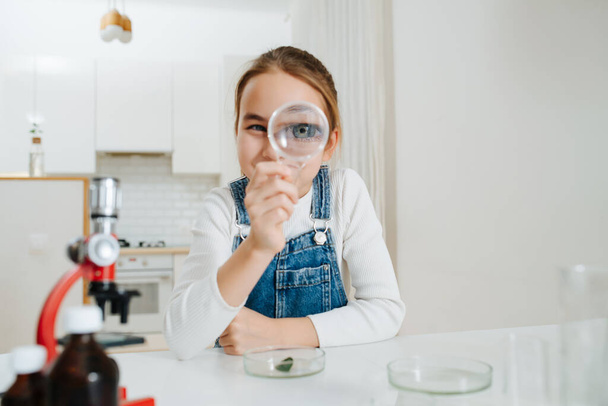 Silly little girl playing with magnifying glass while doing home science project - Фото, изображение