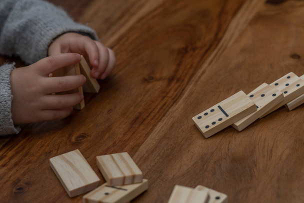 child's hands in gray sweater playing dominoes with blurred focus - Фото, изображение