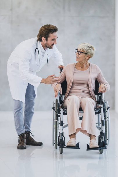 Επιτυχημένος γιατρός μιλάει με την ηλικιωμένη γυναίκα ασθενή με αναπηρική καρέκλα. - Φωτογραφία, εικόνα