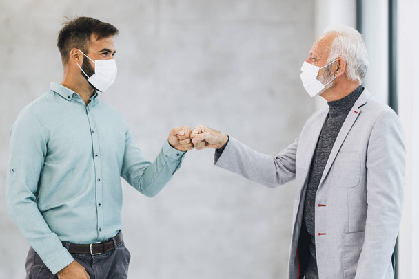 Un saludo de dos hombres de negocios con puños en la oficina durante la pandemia del virus corona para evitar apretones de manos. - Foto, imagen