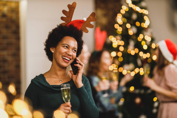 Щаслива афро-американська жінка, яка розмовляє на смартфоні на новорічній вечірці в святковій атмосфері. - Фото, зображення