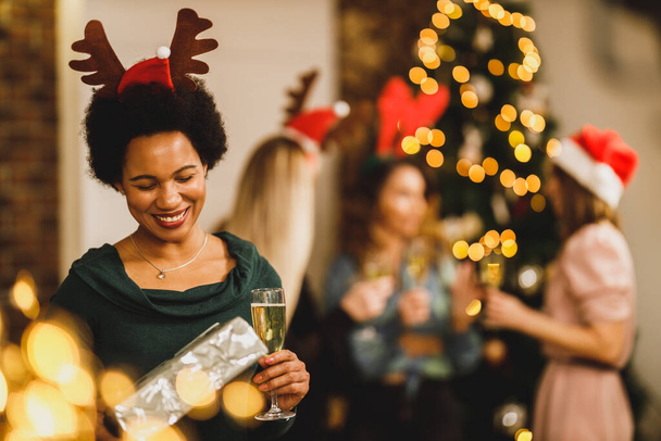Feliz mujer afroamericana trayendo regalos mientras celebra la Navidad con sus amigos en la fiesta en casa. - Foto, imagen
