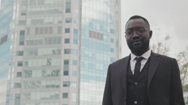 Ritratto palmare di un uomo d'affari afro-americano di successo in abito elegante in piedi su strada in città e guardando la fotocamera - Filmati, video