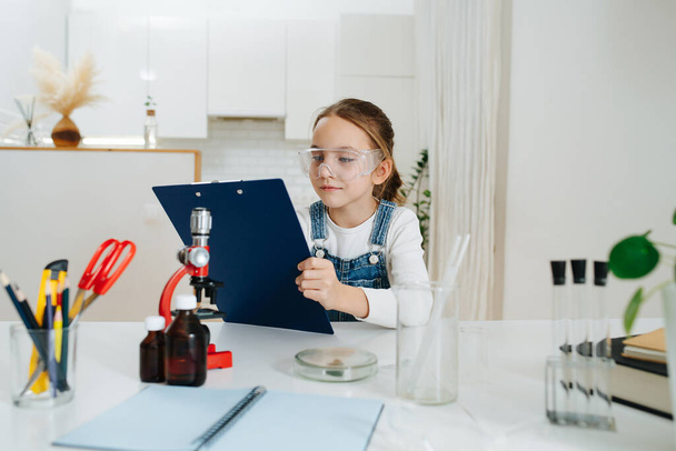 Eight year old girl trying to do home science project, checking her plan - Photo, Image