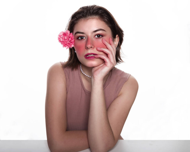 Mladá žena s růžovou květinou. Nenucené ženy drží růžovou květinu za uchem objemné růžové make-up izolované přes bílé pozadí. Koncept krásy a zdravotní péče volný prostor pro text - Fotografie, Obrázek
