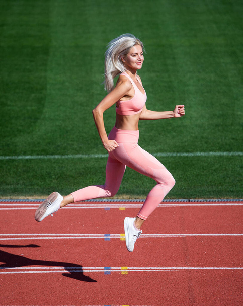 lose weight. speed and energy. stamina. sexy runner in fitness sportswear. sprinting on outdoor arena racetrack. training and workout. athletic female coach running. woman sport trainer in motion - Фото, зображення