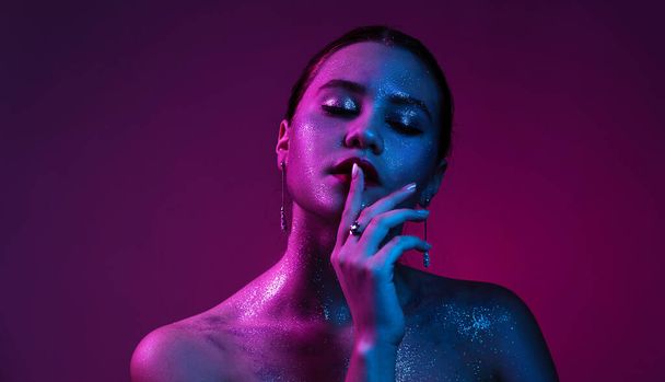 Fashion woman in silver sparkles and colorful bright neon lights posing in studio, portrait of beautiful woman, trendy glowing sequins make up. Art design glitter vivid makeup. - Foto, Imagen