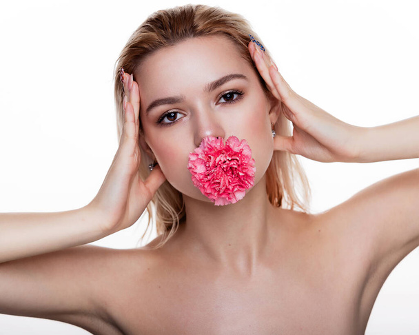 Charmante jonge vrouw met roze bloem in de mond. Blond model met roze bloem geïsoleerd over een witte achtergrond. Begrip schoonheid en gezondheidszorg vrije ruimte voor tekst - Foto, afbeelding