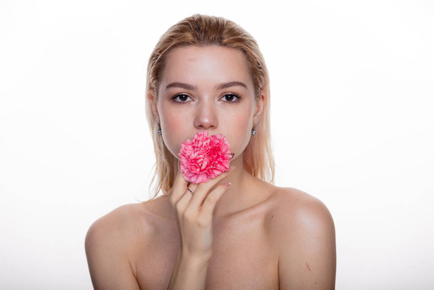 Charming young woman with pink flower in the mouth. Blonde model holding pink flower isolated over white background. Concept of beauty and health care free space for text - Photo, Image