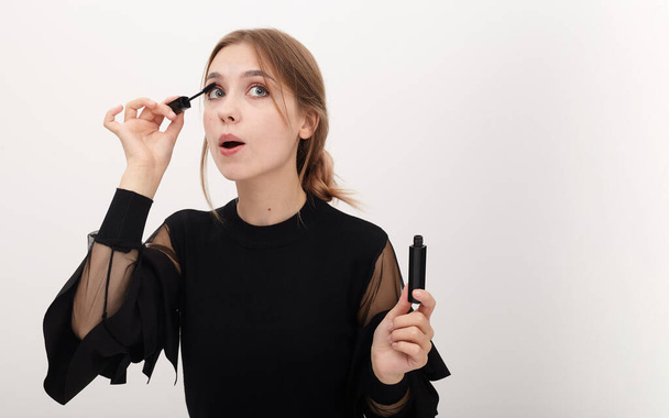 beautiful girl emotionally paints her eyelashes with black mascara - Photo, Image