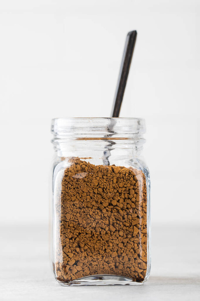 Glass jar with instant coffee with a spoon on a light background. - Foto, Imagen