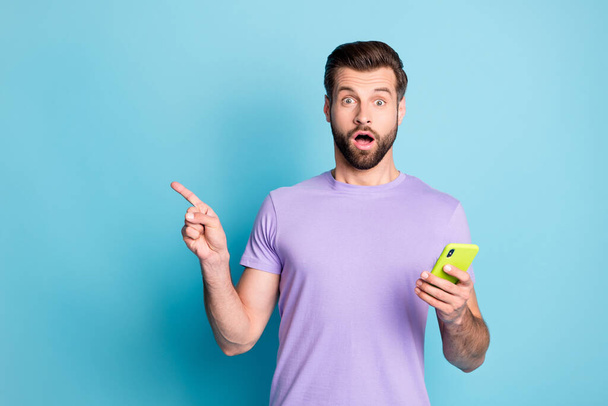 Photo portrait of amazed surprised man showing empty space keeping cellphone isolated vibrant blue color background - Foto, Imagem