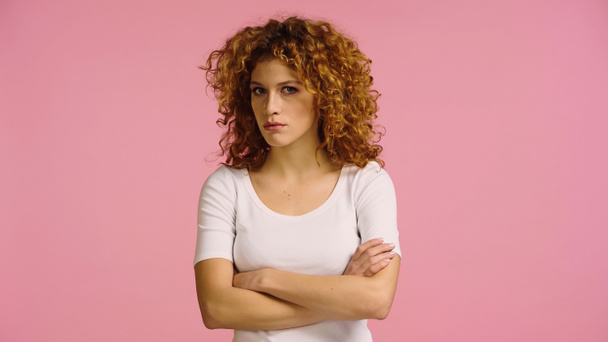 displeased redhead woman in white t-shirt standing with crossed arms isolated on pink - Foto, Bild
