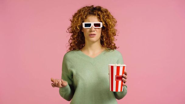 засмучена жінка в 3d окулярах тримає попкорн відро під час перегляду фільму ізольовано на рожевому
 - Фото, зображення