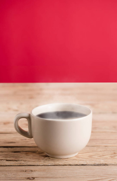 tasse de café blanc cassé avec fumée de vapeur chaude sur table en bois rustique, fond rouge - Photo, image