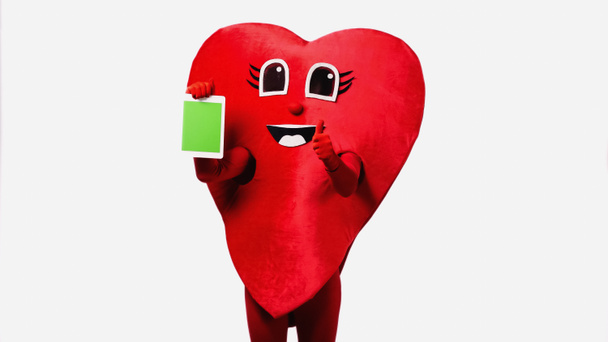 persona en traje de corazón rojo sosteniendo tableta digital con pantalla verde y mostrando el pulgar hacia arriba aislado en blanco - Foto, Imagen