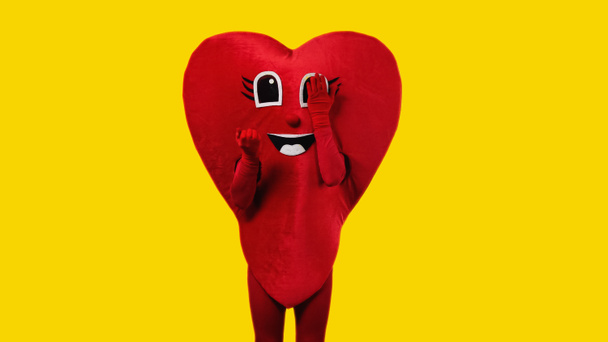 person in heart costume touching cartoon eye isolated on yellow - Fotoğraf, Görsel
