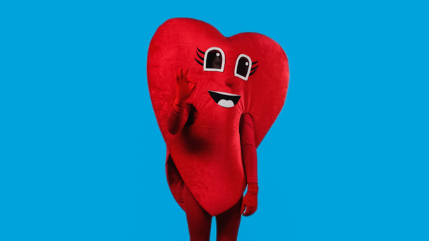 osoba v pozitivním srdečním kostýmu ukazuje v pořádku izolované na modré  - Fotografie, Obrázek