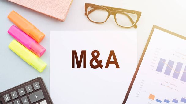 The letters M and S written on notepad. Glasses, calculator and color markers are on white background. M and A short for Mergers and Acquisitions, business concept. - Photo, Image