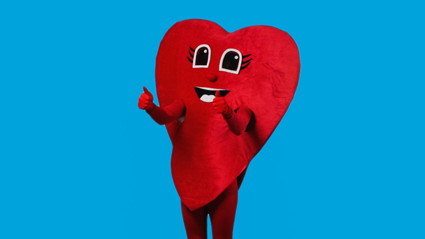 person in joyful heart costume showing thumbs up isolated on blue  - Photo, image