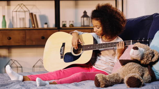 afrikkalainen amerikkalainen lapsi soittaa akustista kitaraa makuuhuoneessa - Valokuva, kuva