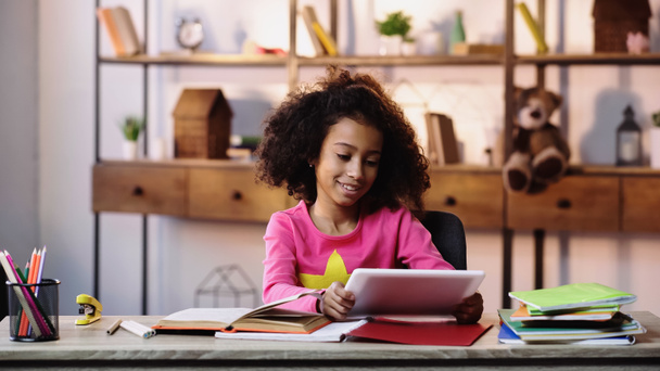щаслива афроамериканська дівчина використовує цифровий планшет біля блокнотів на столі
  - Фото, зображення