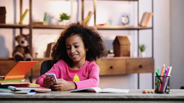 enfant afro-américain joyeux en utilisant un téléphone portable près des ordinateurs portables - Photo, image
