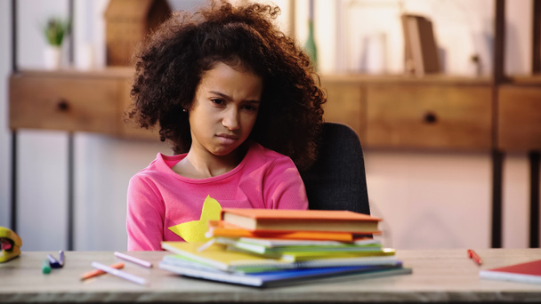 criança americana africana descontente olhando para cadernos enquanto faz lição de casa - Foto, Imagem