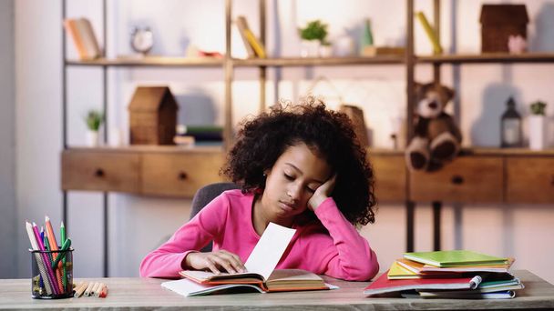 bored african american child looking at book while doing homework  - Фото, изображение