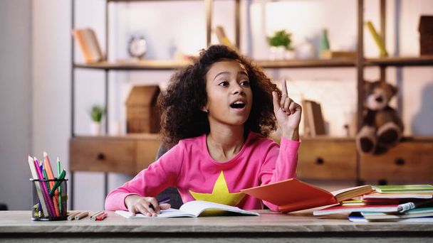 curly african american schoolgirl having idea while doing homework  - Фото, изображение