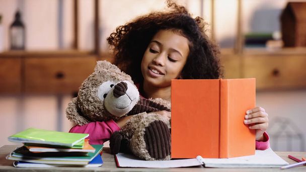 happy african american girl reading book to teddy bear  - Foto, Bild