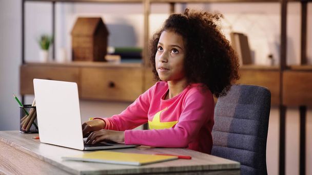 töprengő afro-amerikai iskolás gyerek használja laptop, miközben a házi feladatot  - Fotó, kép