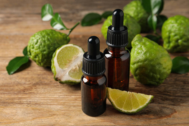 Bottles of essential oil and fresh bergamot fruits on wooden table - Фото, изображение