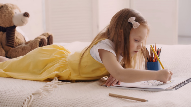 Child drawing with color pencil near teddy bear on bed  - Valokuva, kuva