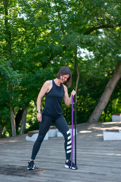 Mujer fitness haciendo ejercicio para bíceps con banda de resistencia al aire libre. Entrenamiento de chica atlética - Foto, imagen