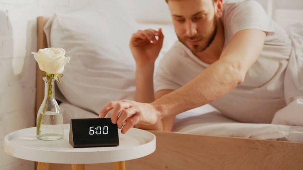 Blurred man turning off clock near flower on bedside table  - Photo, Image